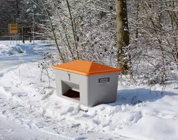 Il bidone della ghiaia CEMO con apertura di rimozione si trova sul bordo di una strada coperta di neve.